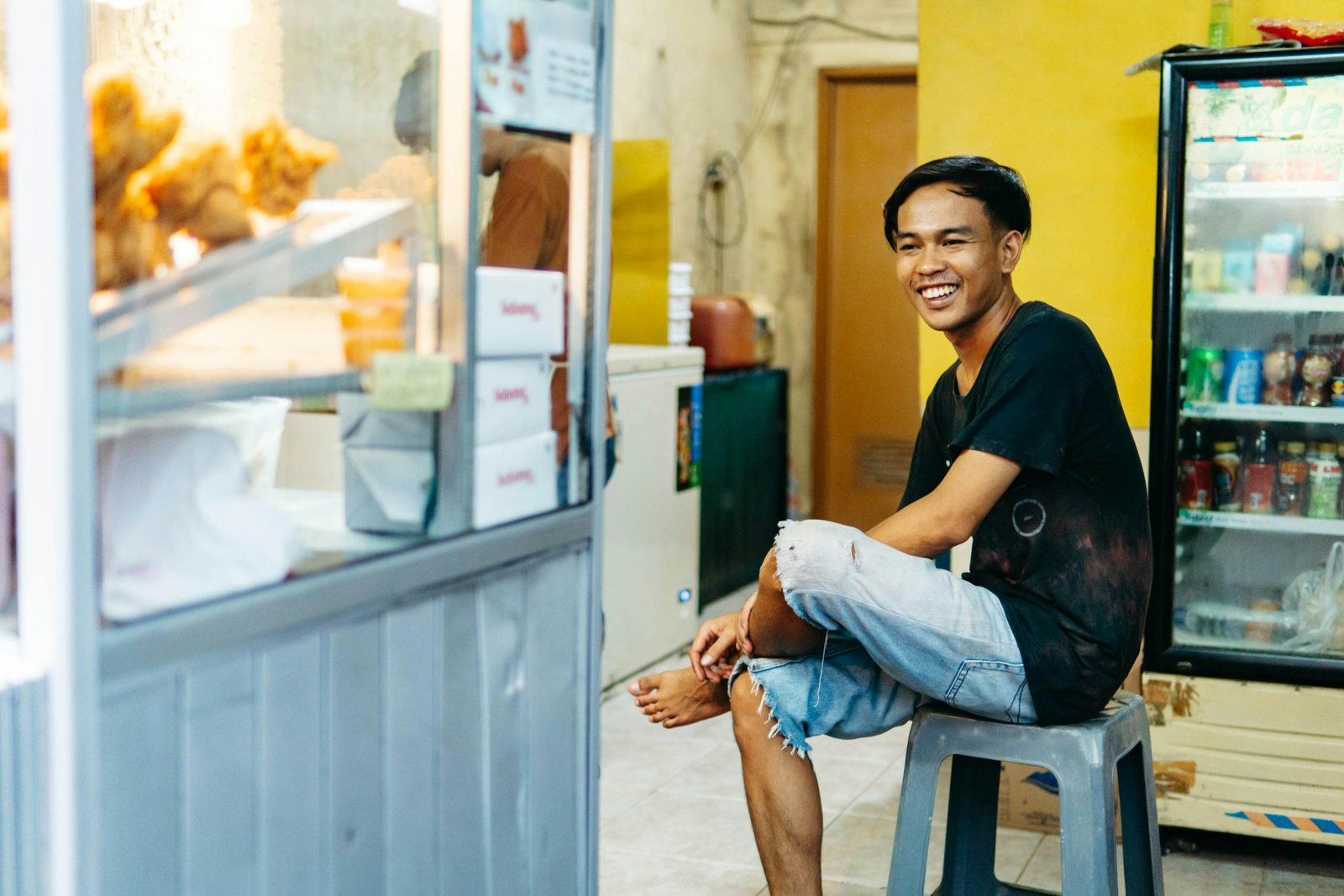 Casual portrait of a smiling young man sitting indoors in a small street store.